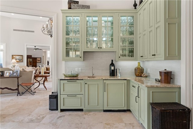 bar featuring tasteful backsplash, light stone counters, sink, an inviting chandelier, and green cabinetry