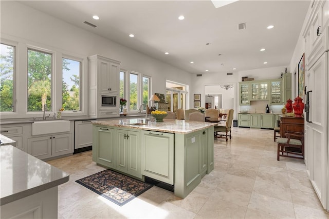 kitchen with stainless steel microwave, sink, green cabinets, white dishwasher, and a kitchen island with sink