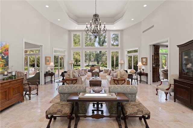 living room featuring a chandelier, a high ceiling, a raised ceiling, and a healthy amount of sunlight