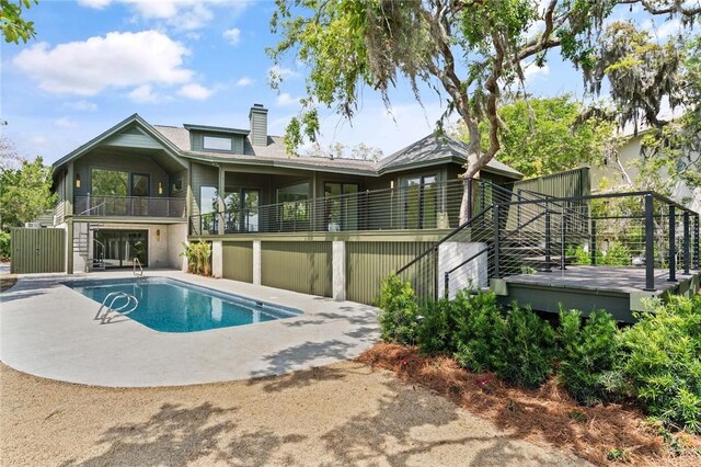 rear view of house featuring a chimney, stairs, an outdoor pool, a balcony, and a patio
