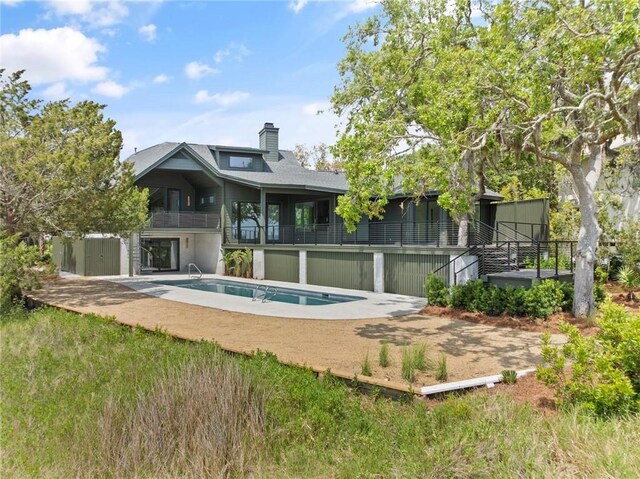 rear view of house with a wooden deck, a shingled roof, a chimney, and an outdoor pool