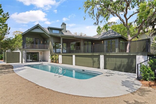 rear view of house with a chimney, an outdoor pool, a patio area, and a balcony