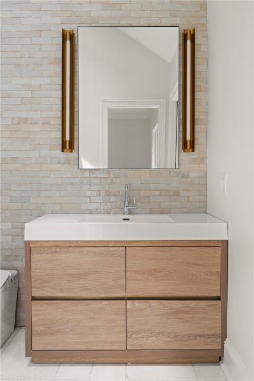 bathroom featuring tile patterned floors, toilet, vanity, baseboards, and tasteful backsplash