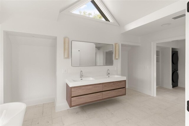 full bath featuring stacked washer / dryer, vaulted ceiling, a sink, and double vanity