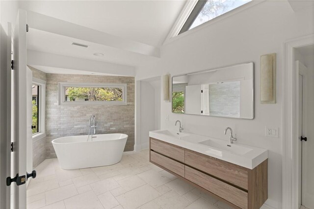 full bath featuring a freestanding bath, visible vents, a sink, and double vanity