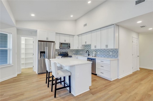 kitchen featuring a center island, stainless steel appliances, a kitchen breakfast bar, light hardwood / wood-style flooring, and white cabinets