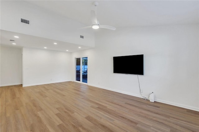 unfurnished living room with ceiling fan, a towering ceiling, and light wood-type flooring