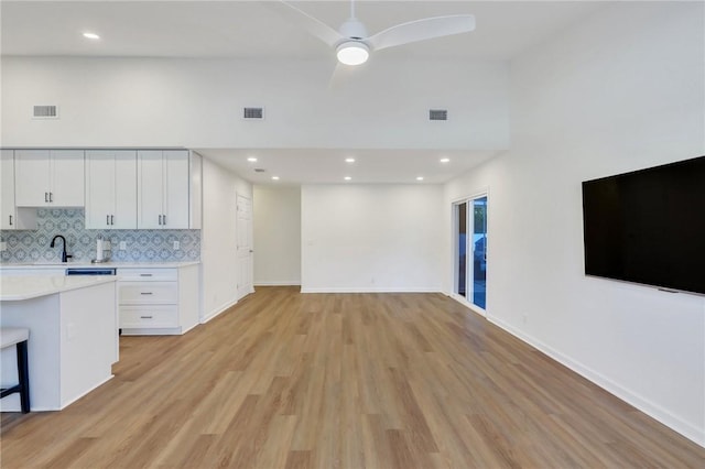 kitchen featuring backsplash, a towering ceiling, light hardwood / wood-style flooring, and white cabinets