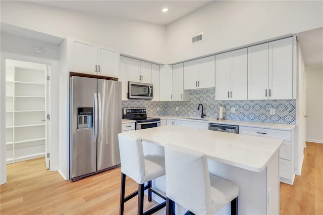 kitchen with sink, a kitchen island, appliances with stainless steel finishes, light hardwood / wood-style floors, and white cabinetry