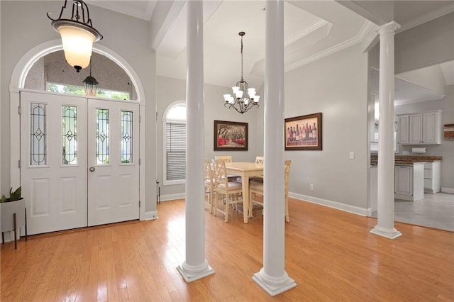 entrance foyer with light wood finished floors, baseboards, a towering ceiling, ornate columns, and ornamental molding