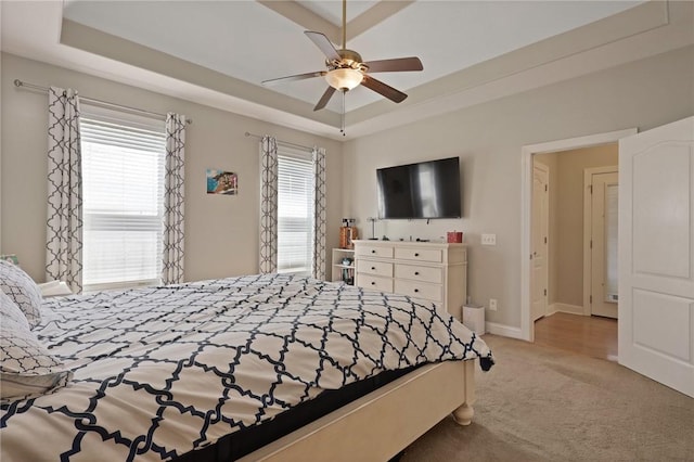 bedroom featuring a tray ceiling, light carpet, baseboards, and multiple windows