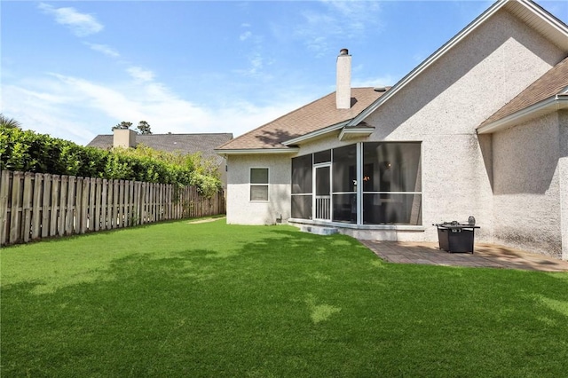 rear view of property with a chimney, a sunroom, a fenced backyard, a yard, and stucco siding