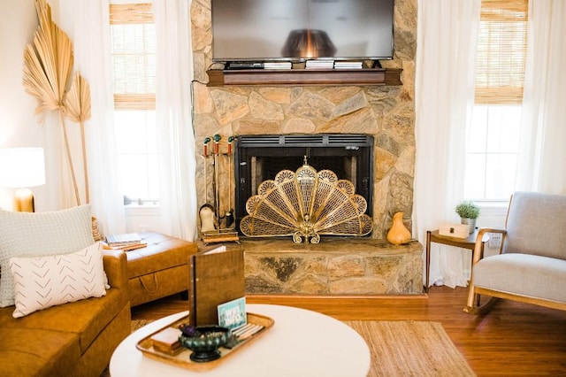 living area featuring wood-type flooring, a stone fireplace, and a wealth of natural light