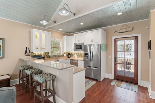 622 Beachview Dr, Saint Simons Island, GA 31522 - kitchen with appliances with stainless steel finishes, a peninsula, white cabinets, light stone countertops, and a kitchen breakfast bar
