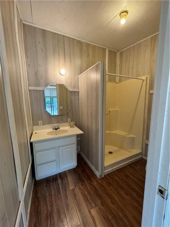 bathroom featuring a textured ceiling, vanity, a shower, hardwood / wood-style flooring, and wood walls