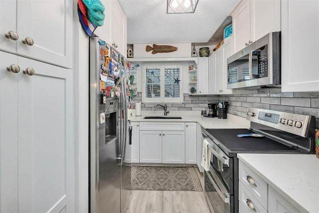 kitchen with sink, light hardwood / wood-style floors, a textured ceiling, white cabinets, and appliances with stainless steel finishes