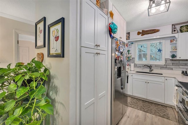 kitchen with a textured ceiling, stainless steel appliances, sink, light hardwood / wood-style floors, and white cabinetry