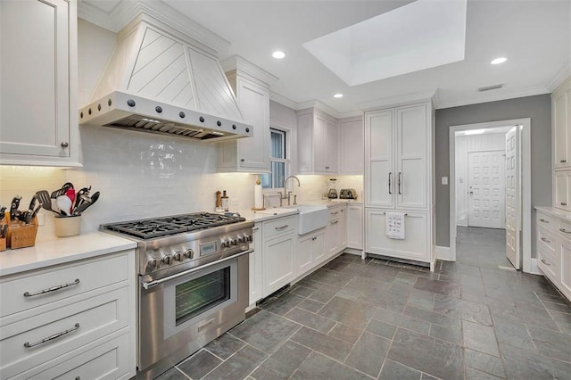 kitchen with a sink, white cabinets, wall chimney exhaust hood, stainless steel range, and crown molding