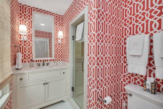 bathroom with vanity, a shower stall, toilet, and wallpapered walls