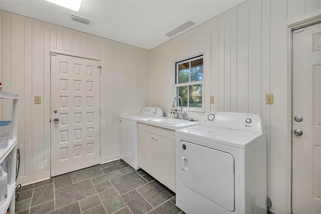 laundry area with cabinet space, visible vents, washing machine and dryer, a sink, and wooden walls