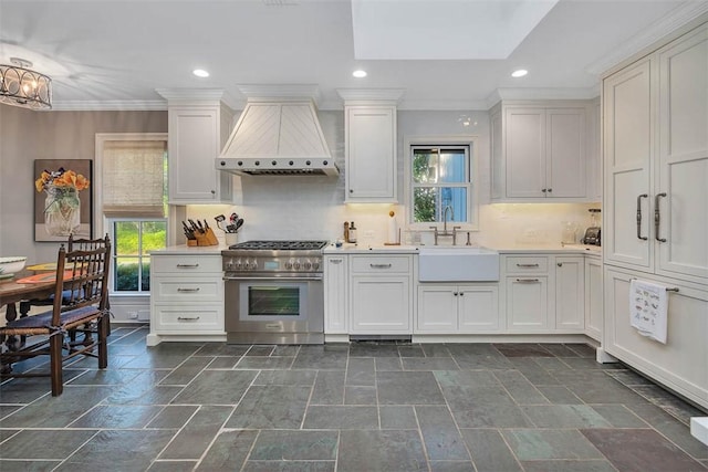 kitchen with high end stainless steel range oven, stone finish flooring, light countertops, wall chimney range hood, and a sink