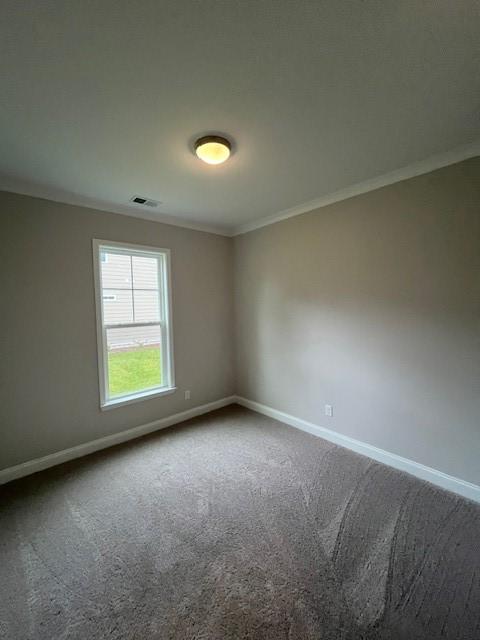 spare room featuring baseboards, ornamental molding, and dark colored carpet
