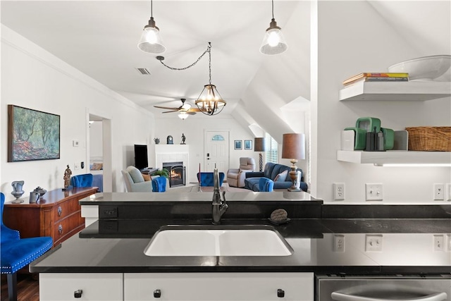 kitchen with white cabinets, dark countertops, a tiled fireplace, and a sink