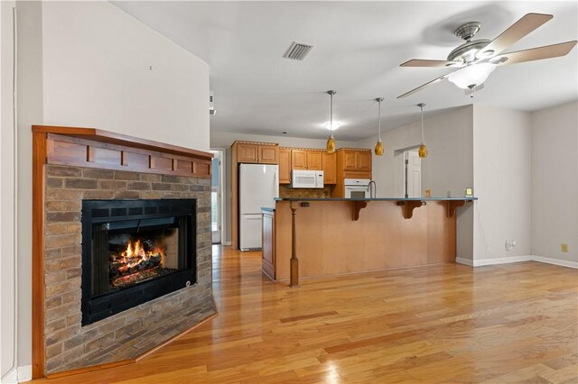 kitchen featuring kitchen peninsula, light hardwood / wood-style floors, white appliances, a kitchen bar, and a fireplace