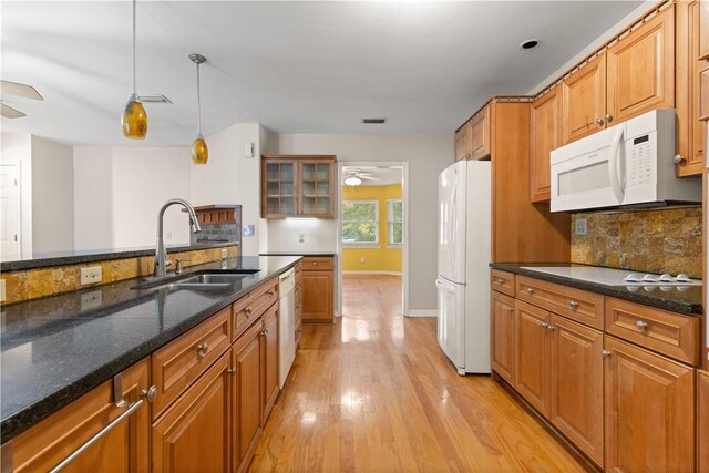 kitchen with pendant lighting, white appliances, dark stone counters, sink, and light hardwood / wood-style floors