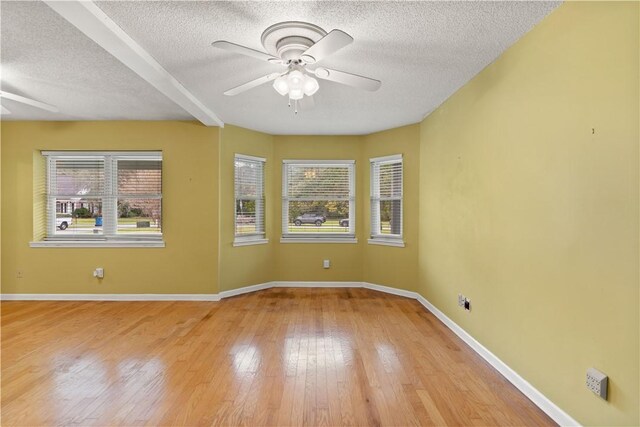 unfurnished room featuring beam ceiling, a textured ceiling, light hardwood / wood-style floors, and ceiling fan