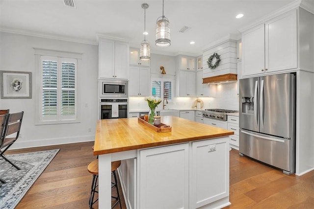 kitchen with appliances with stainless steel finishes, backsplash, a kitchen island, pendant lighting, and white cabinetry