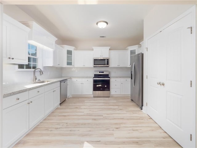 kitchen with white cabinets, appliances with stainless steel finishes, light wood-type flooring, and light stone countertops