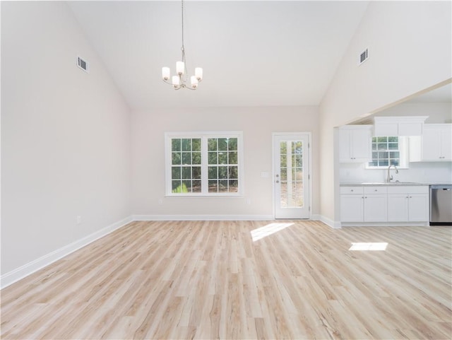 unfurnished living room with light hardwood / wood-style flooring, high vaulted ceiling, a chandelier, and sink