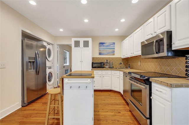 kitchen with stainless steel appliances, a kitchen island, white cabinetry, and stacked washer / dryer