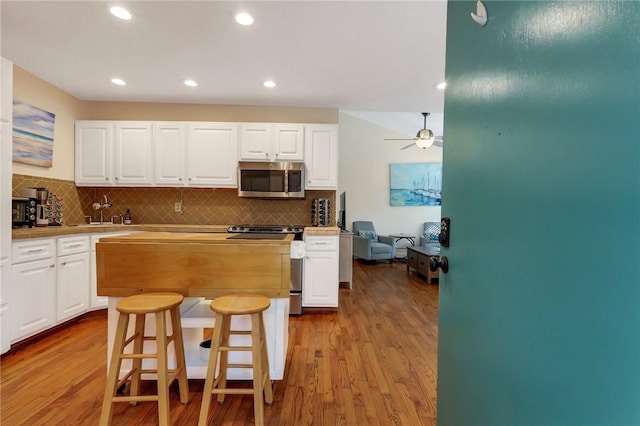 kitchen with a kitchen breakfast bar, light wood-type flooring, backsplash, stainless steel appliances, and white cabinetry