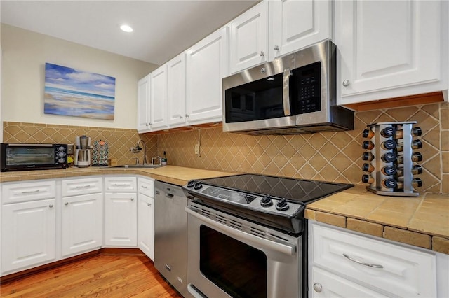 kitchen featuring light wood-type flooring, tasteful backsplash, stainless steel appliances, sink, and white cabinetry