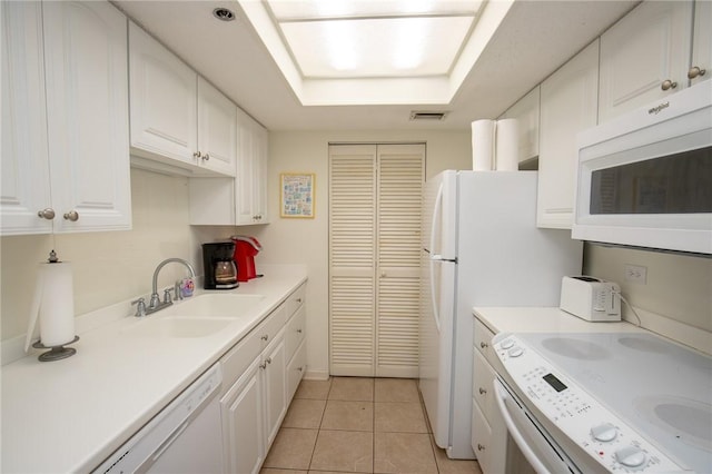 kitchen featuring white appliances, visible vents, a tray ceiling, a sink, and white cabinets