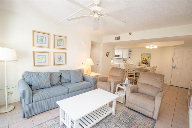 living room featuring light tile patterned flooring, visible vents, ceiling fan with notable chandelier, and a textured ceiling