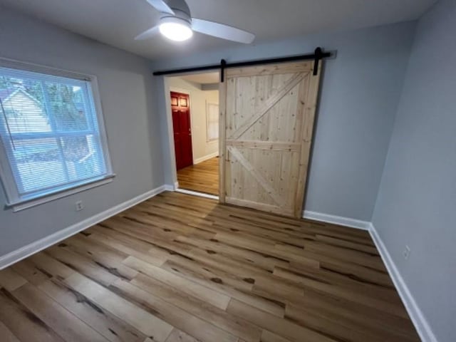 unfurnished bedroom featuring wood-type flooring, a barn door, and ceiling fan