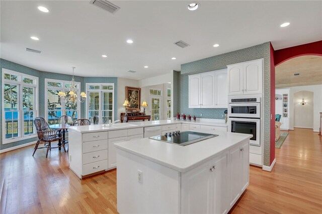 kitchen with hanging light fixtures, double oven, kitchen peninsula, black electric cooktop, and light wood-type flooring