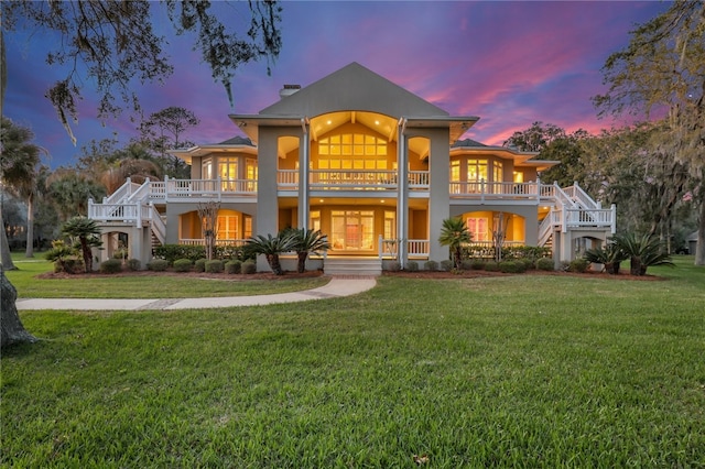 back house at dusk with a lawn and covered porch