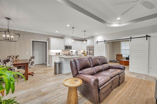 living room featuring recessed lighting, a barn door, light wood-style floors, ornamental molding, and ceiling fan with notable chandelier