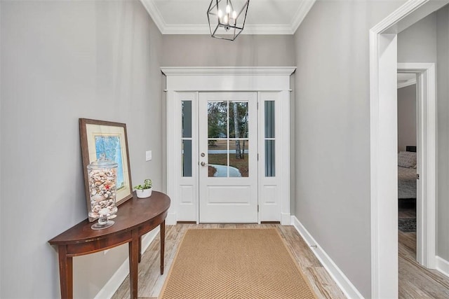 entryway featuring light wood-type flooring, a notable chandelier, crown molding, and baseboards