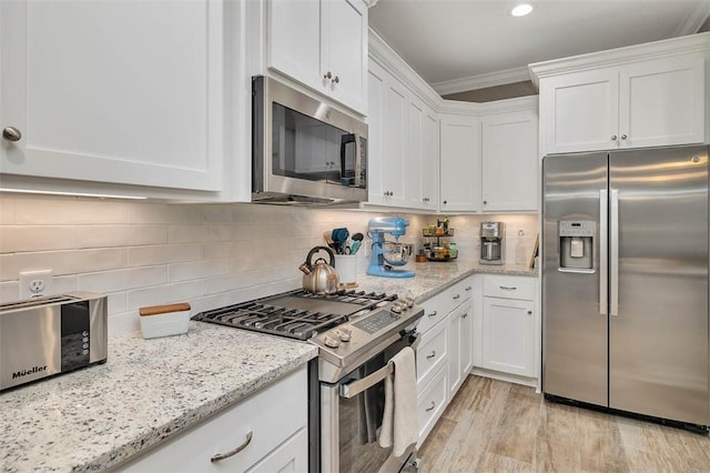 kitchen featuring white cabinets, ornamental molding, appliances with stainless steel finishes, backsplash, and light wood finished floors