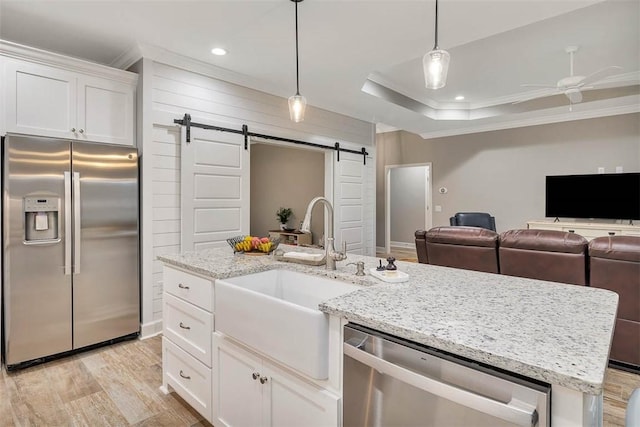 kitchen featuring a barn door, a kitchen island with sink, a sink, appliances with stainless steel finishes, and a raised ceiling