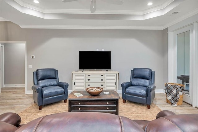 living area featuring a tray ceiling, wood finished floors, and ornamental molding