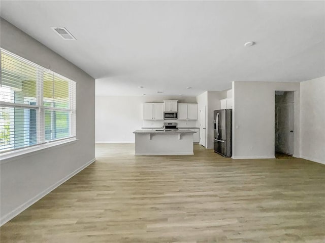 unfurnished living room with light wood-style flooring, baseboards, and visible vents