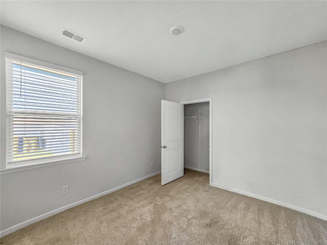 unfurnished bedroom featuring light colored carpet, visible vents, a closet, and baseboards