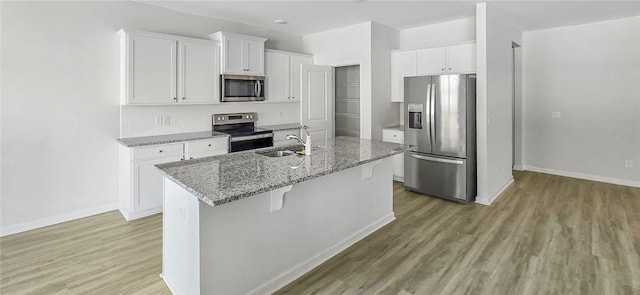 kitchen featuring light wood-type flooring, a center island with sink, a sink, appliances with stainless steel finishes, and white cabinets