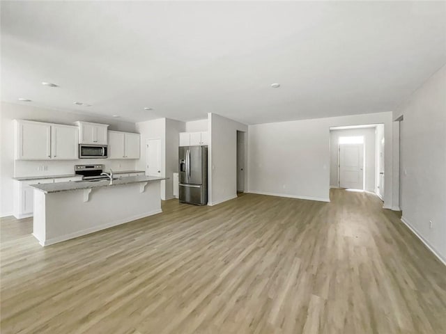 kitchen featuring light wood finished floors, an island with sink, white cabinets, appliances with stainless steel finishes, and a kitchen breakfast bar